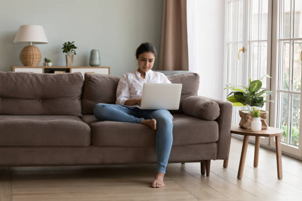 istock Serious Indian woman use laptop texting e-mail seated on couch 1435907694