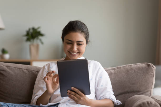 istock Indian woman sits on sofa with modern digital tablet device 1435907704