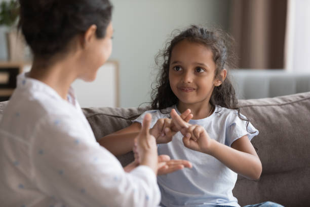 Deaf Indian girl and mother communicating using sign language Deaf Indian preschooler girl and young mother showing symbols with hands using visual-manual gestures enjoy communication seated on couch at home. Hearing loss and disability, sign language usage american sign language stock pictures, royalty-free photos & images