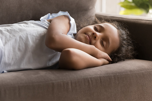 Little Indian girl sleeps on sofa at home, close up. Cute serene preschooler child fall asleep on couch, enjoy daytime nap, take break during day, resting alone indoor. Children growth, healthy sleep