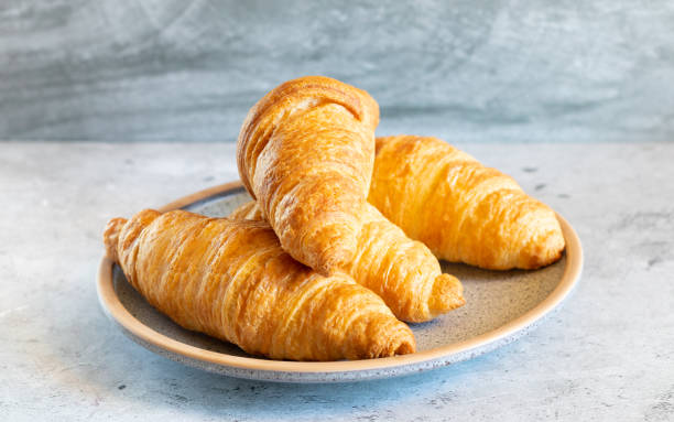 istock Four croissants on ceramic plate on light concrete background close-up side view 1435909601
