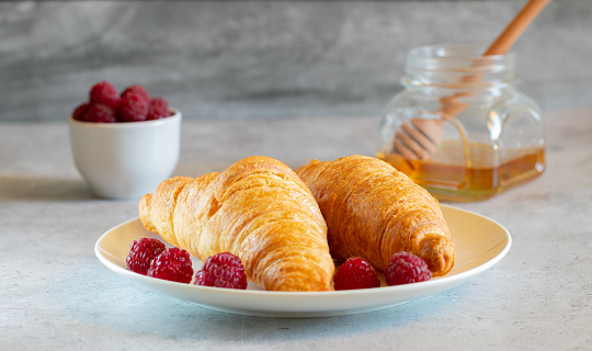 Two croissants with raspberries and honey on a light concrete background. Side view, close-up, horizontal.