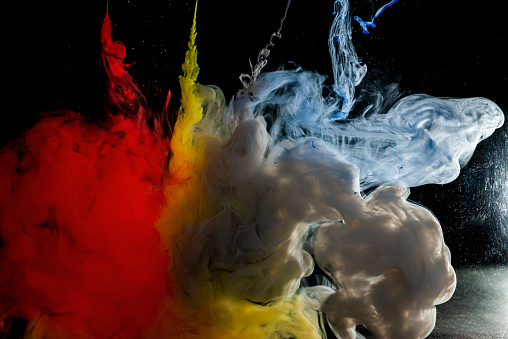 A needles from which the red, yellow, blue and gray paint flows into bowl of water on a black background