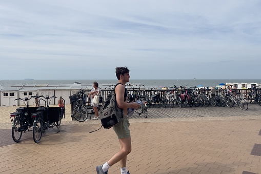 Knokke, Belgium – September 01, 2022: A man walking by parked bikes next to the White beach huts in the small Belgian town of Knokke-Heist