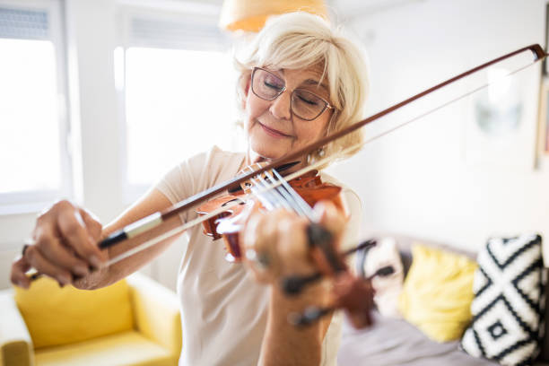 senior woman with eyes closed playing violin at home - violin family imagens e fotografias de stock