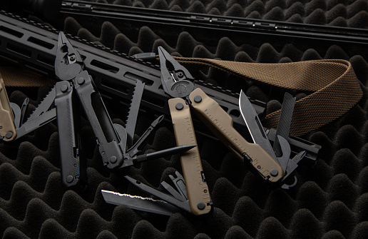Modern multitool with many tools. A portable multi-tasking military tool lies next to the weapon. Dark background.