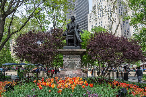 New York City, United States of America - May 4, 2017. Statue of William H. Seward by artist Randolph Rogers, located in Madison Square Park in Manhattan, New York. Dedicated on September 27, 1876, it is believed to be the city's first monument depicting a New York resident. The portrait statue is set on a red Levante marble pedestal. William Henry Seward (18011872) was an American politician who served as United States Secretary of State from 1861 to 1869, and earlier served as governor of New York and as a United States Senator. View with people and flowers.