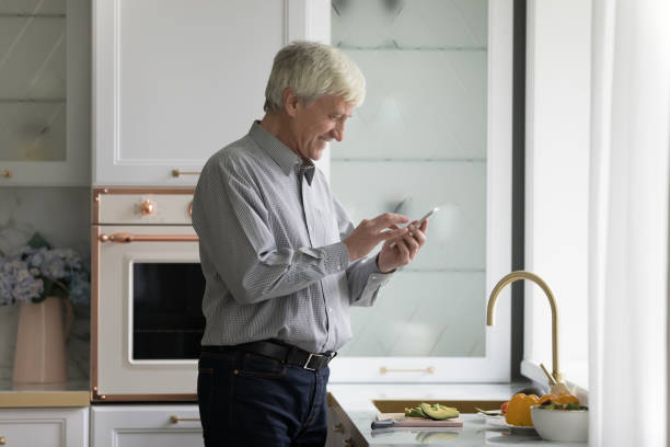 istock Elderly man holds smartphone text message standing in modern kitchen 1435938865