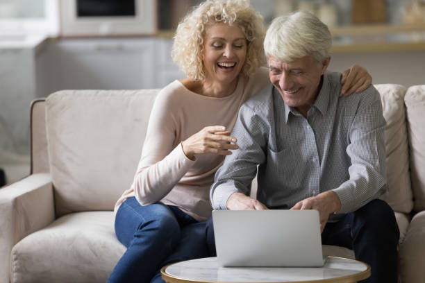 istock Older couple sit on sofa laughing staring at laptop screen 1435938869