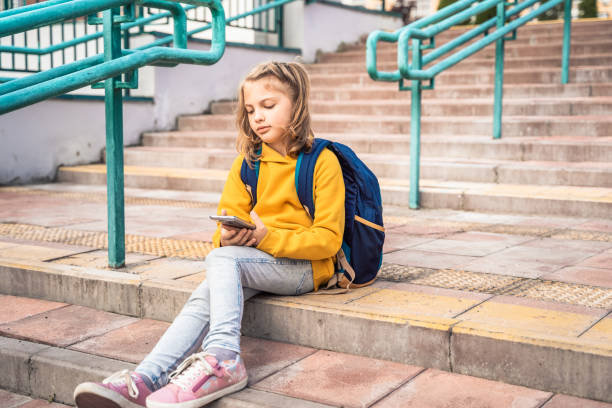 istock Back to elementary, primary school. Little girl with backpack,mobile phone. Chat, talk with friends, classmates on break. Autumn study after vacation. Education of children. Pupil kid on stair steps 1435951489