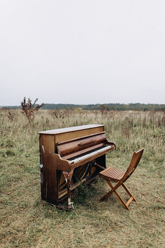 A lonely piano stands in a field in cloudy weather
