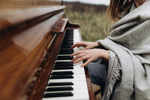 Beautiful female hands play the keys of a piano located in a field in cloudy weather in autumn