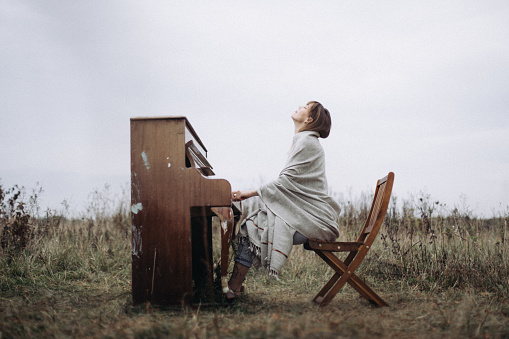 A beautiful woman is playing the piano with pleasure in a field in autumn