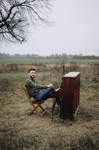 A handsome man sits at the piano in a field in cloudy autumn weather