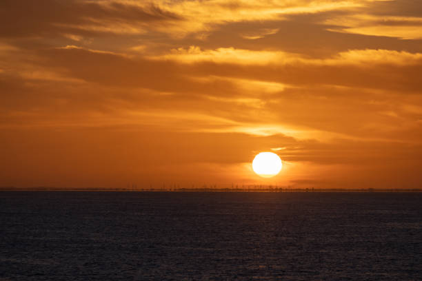 Dramatic sunrise and cloud formations over the sea near Dover, Southern England with a distant windmill farm sitting along the horizon line being illuminated by the rising sun stock photo