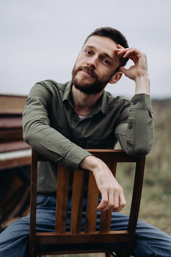 A handsome man is sitting on a chair in a field in cloudy autumn weather at the piano on the background