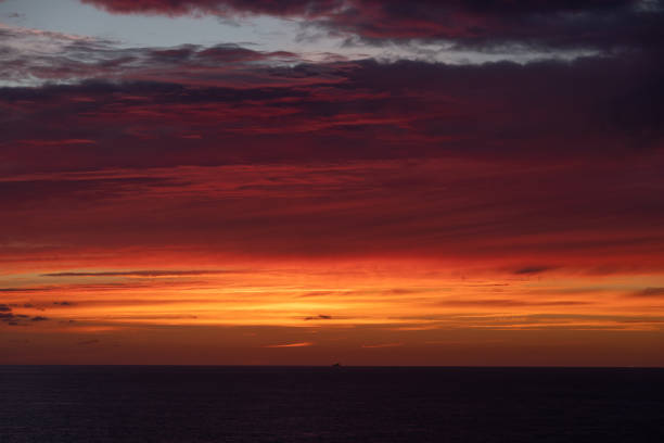 Dramatic sunrise and cloud formations over the sea near Dover, Southern England with a distant ship sitting along the horizon line being illuminated by the rising sun