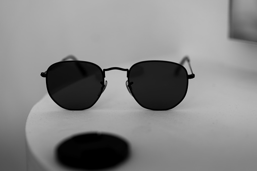 A closeup black and white shot of sunglasses on white table with dark spot on it