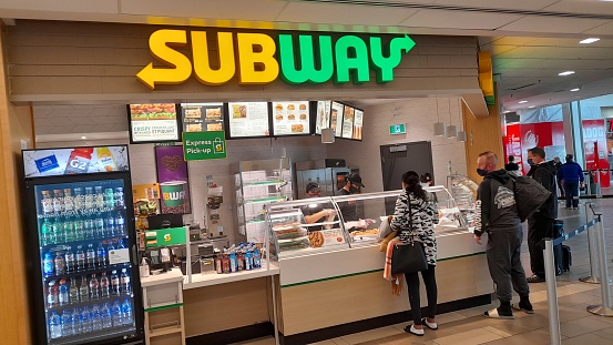 Advertisement Sign, People Wearing Face Mask Due To Coronavirus, Standing In Front Of Subway Restaurant, Buying Food And Drink Scenery At Vancouver International Airport Canada