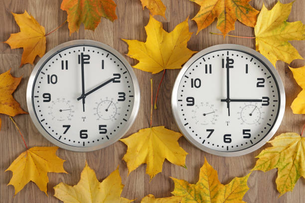 deux horloges, l’une indique deux heures, l’autre trois heures. des feuilles d’automne tombées jaunes traînent. - minute hand number 15 clock time photos et images de collection