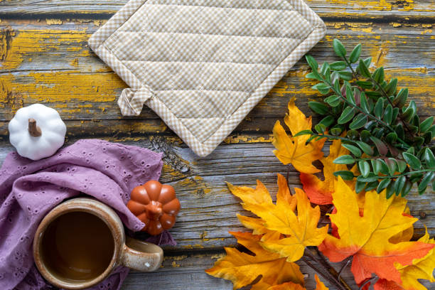 Cozy coffee autumn flat lay arrangement, with pumpkins, pot holder and maple leaves on a yellow rustic wood background stock photo