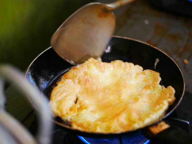 Frying eggs in a wok pan with heat from a gas stove fire in the kitchen. stock photo