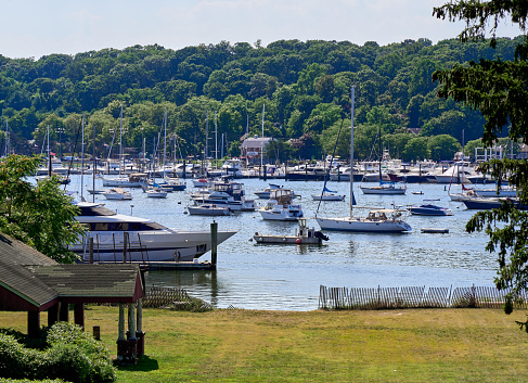 Huntington, NY USA - Aug 19, 2022: Boats in Huntington Harbor on a summer day. In the foreground is Halesite Park. Trees fill the west shore behind the boats in this narrow bay.