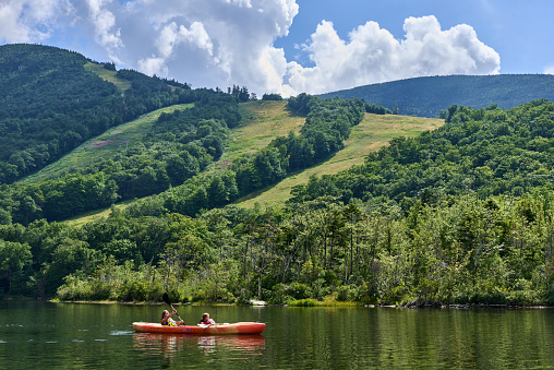 Franconia, NH USA - August 5, 2022: Kayakers on Echo Lake. Behind are ski trails of Cannon Mountain Ski resort in the summer time with a blue sky and dramatic clouds.