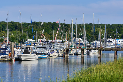 Halesite, NY USA - Aug 19, 2022: Boats in a marina in Huntington Harbor, NY A short pier leads to the boat slips. Sea grass is in the foreground.