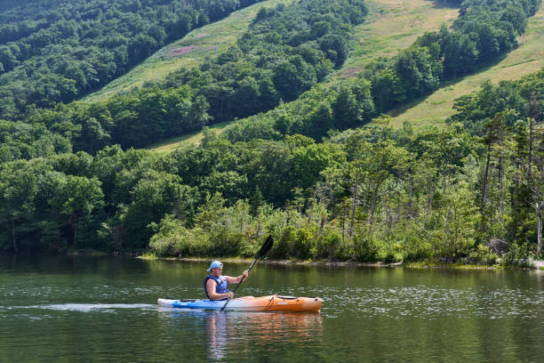 A kayaker on Echo Lake, Franconia, NH Franconia, NH USA - August 5, 2022: A kayaker on Echo Lake. Behind are the ski trails of Cannon Mountain Ski Resort in the summer. franconia new hampshire stock pictures, royalty-free photos & images