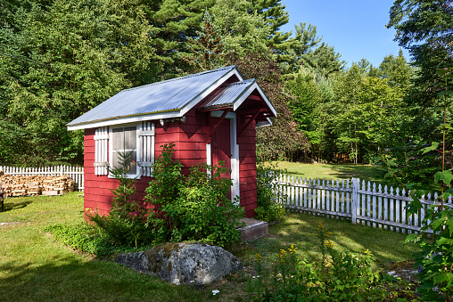 Carroll, NH USA - August 3, 2022: A tiny red cabin and white picket fence the the back yard of a house in the White Mountains of NH.