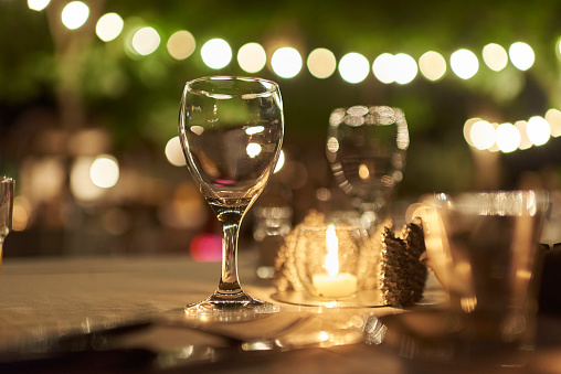 Outdoor celebration night scene, table with glasses and a candle, decoration with strings of lights.