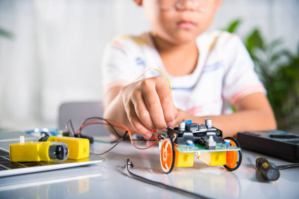 istock Asian kid boy plugging energy and signal cable to sensor chip with open-source hardware and software robot car 1435996397