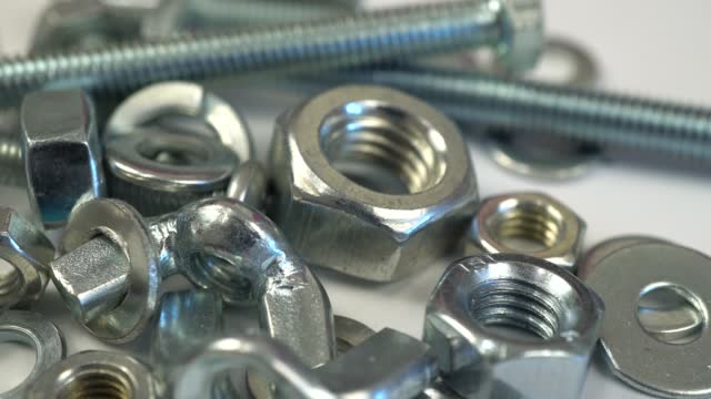 Slide shot of metal bolts and nuts on a white background. Slow macro dolly of a set of fasteners. Metal industry concept.