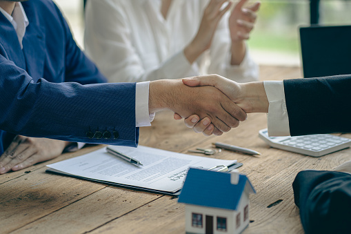 A home agent shakes hands with a customer after signing a contract to buy a home or rent it in the real estate agent's office.