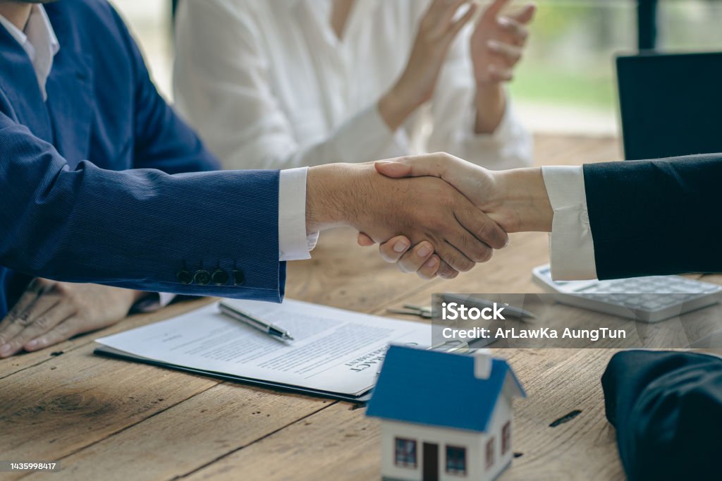 A home agent shakes hands with a customer after signing a contract to buy a home or rent it in the real estate agent's office. Insurance Stock Photo