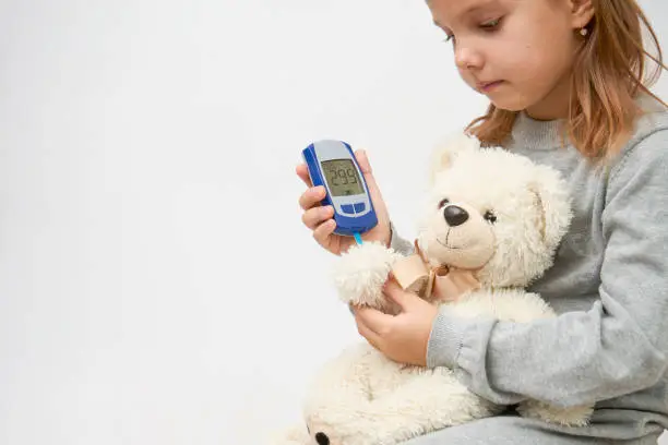 Children and diabetes concept with little girl checking diabetes test to toy bear.