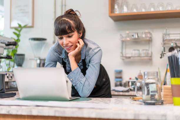 istock Beautiful female barista owner in apron checking online order from customer on computer tablet at coffee shop.Small business concept 1436003214