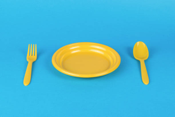 Fork, spoon and plate are yellow on a blue background. Minimal concept of plastic tableware.