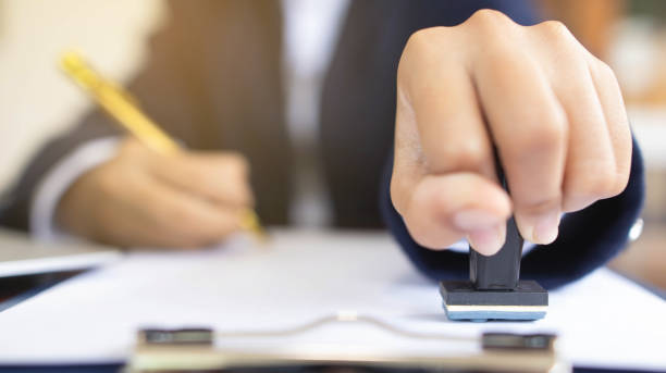 Close-up of a person's hand stamping on an approved application form and approved contract form on paperwork at desk or a businessman working from home isolated for COVID-19 prevention. primer plano de la mano de una persona estampando en un formulario de solicitud aprobado y un formulario de contrato aprobado en el papeleo en el escritorio o un hombre de negocios que trabaja desde casa aislado para la prevención de covid-19.