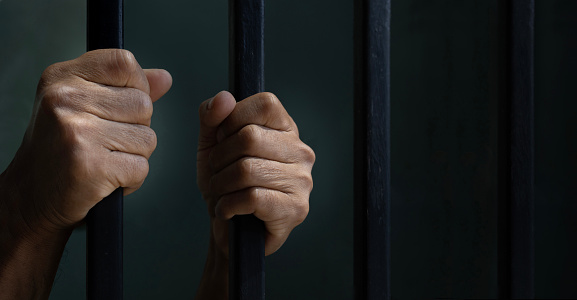 Hand of convicted prisoner behind the cell bar inside jail for incarceration, criminal and limited freedom