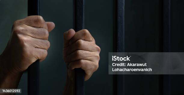 Hand Of Convicted Prisoner Behind The Cell Bar Inside Jail For Incarceration Criminal And Limited Freedom Concept Stock Photo - Download Image Now