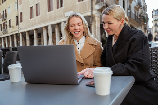 Online. Two blonde women sitting at the laptop in a street cafe