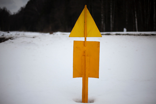 Yellow sign in snow. Steel pole in ground. Warning signal. Pipeline mark.