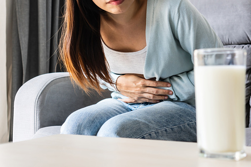 Unhappy young Asian woman having bad stomach ache with glass of milk on table. Lactose intolerance, food allergy concept. Close up, copy space
