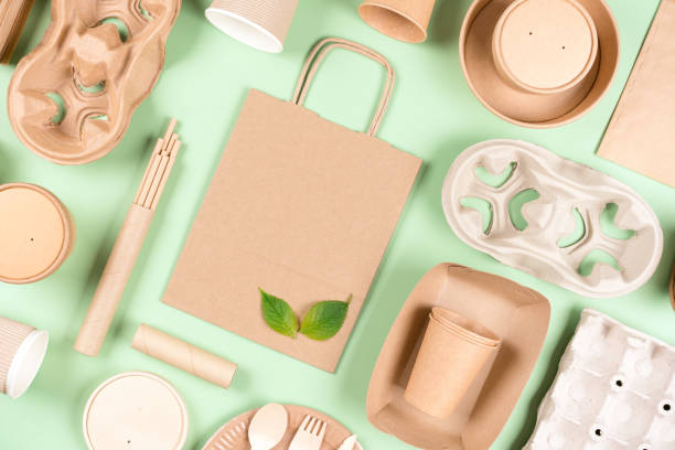 istock Eco paper utensils bundle - food containers, paper bag and cup holders, coffee cups over light green background. Sustainable food packaging concept. Flay lay style 1436025094