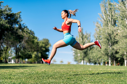 Strong asian woman with sports clothes working out in the park during sunny day. She is jumping in the air.