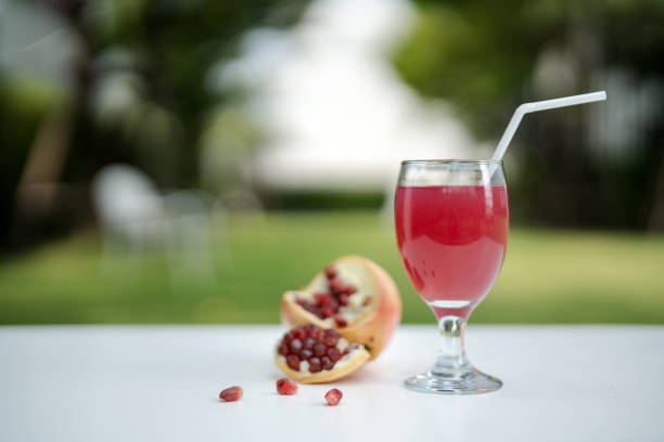 Pomegranate juice with fresh fruit on white wooden table against nature garden background.