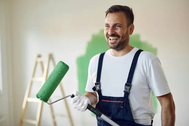 Happy male worker painting the wall in green color during home renovation process.