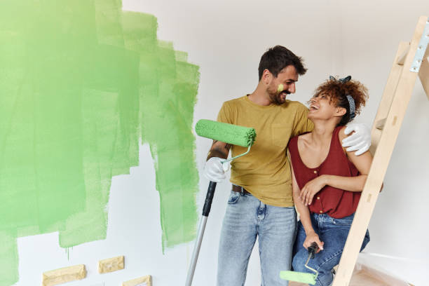 happy couple talking while painting their new apartment. - repairing apartment home improvement painting imagens e fotografias de stock